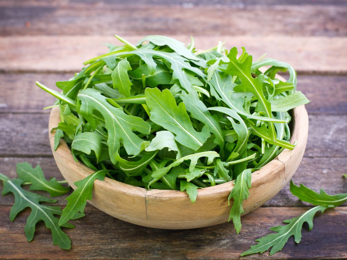 A wooden bowl full of fresh arugula leaves on a wooden table.