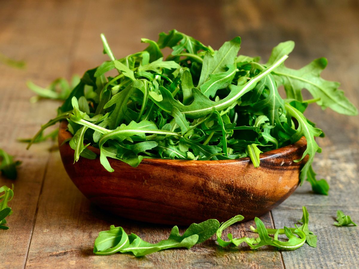 A wooden bowl full of arugula leaves on a table.