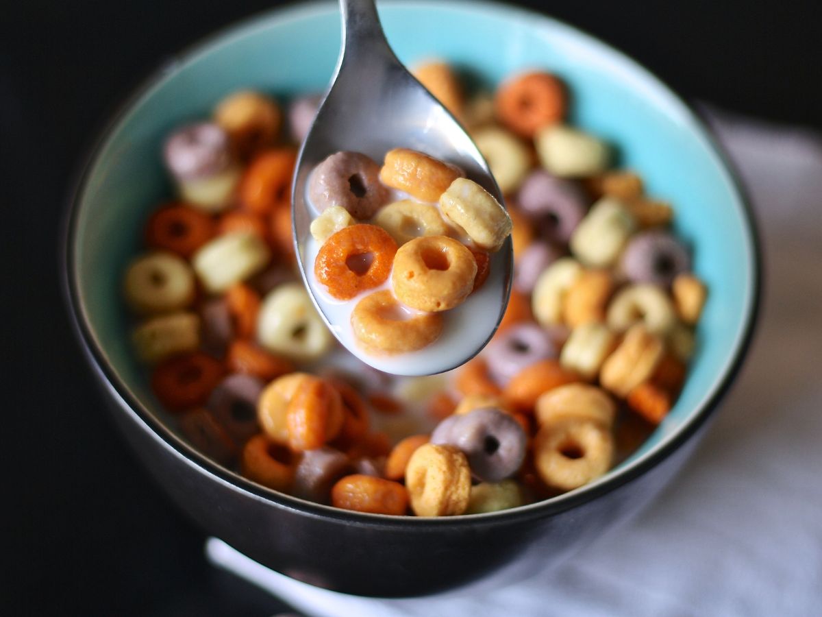 A spoon full of milk and cheerios over a bowl of Cheerios.