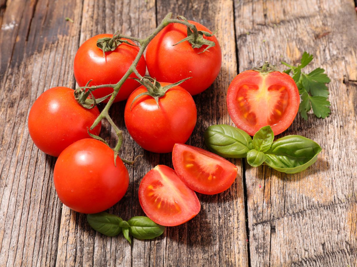 Bunch of fresh ripe cherry tomatoes on a wooden table with leaves and sliced tomatoes.