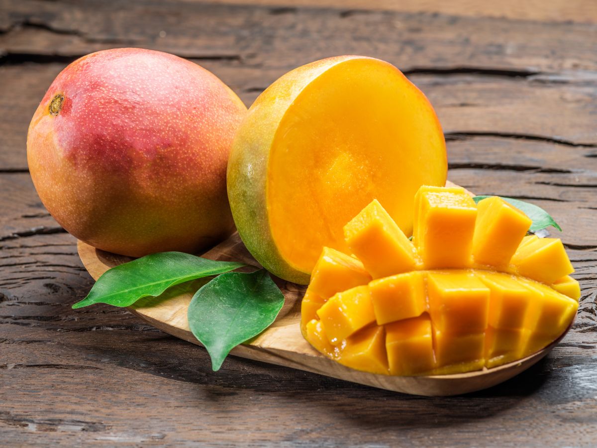 Sliced and whole mango on a wooden cutting board.