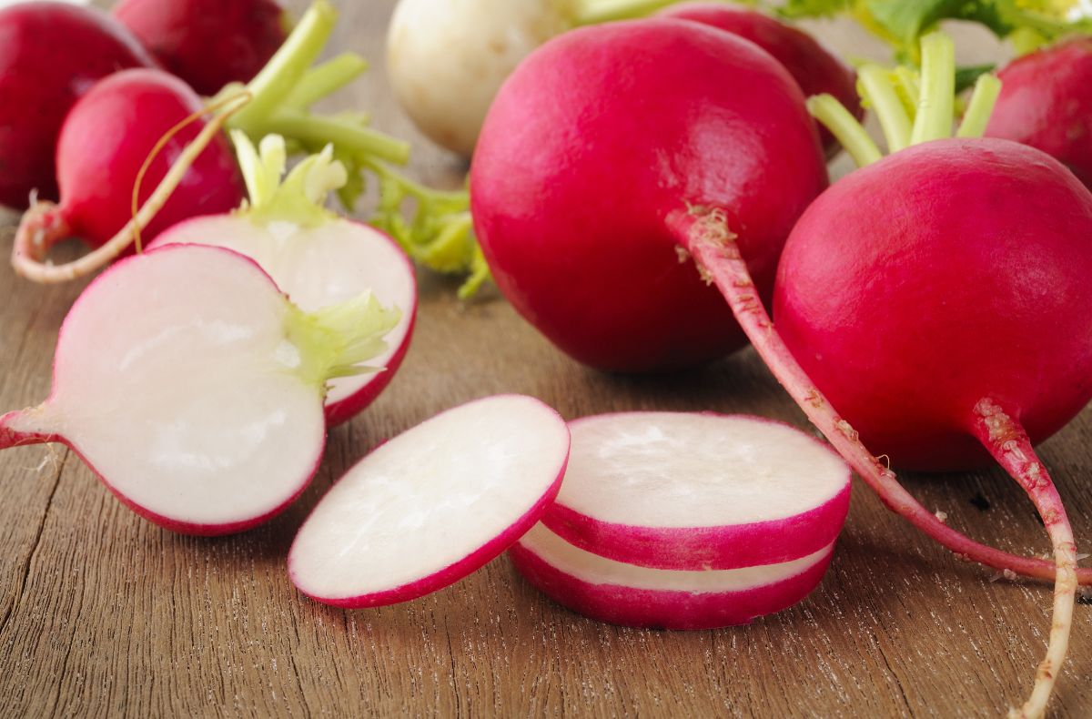 Whole and sliced radishes on a wooden table.