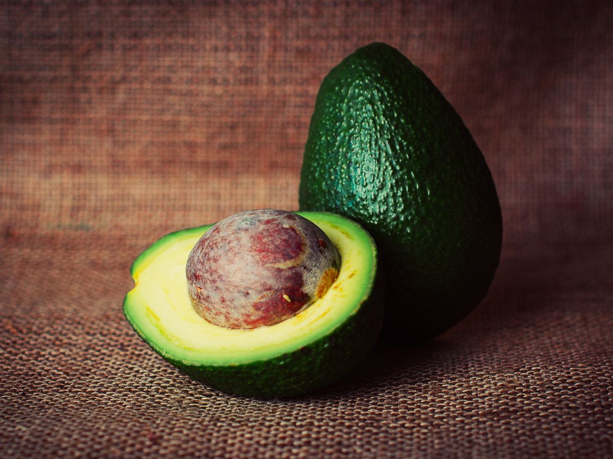 Whole and half of avocado with a pit.