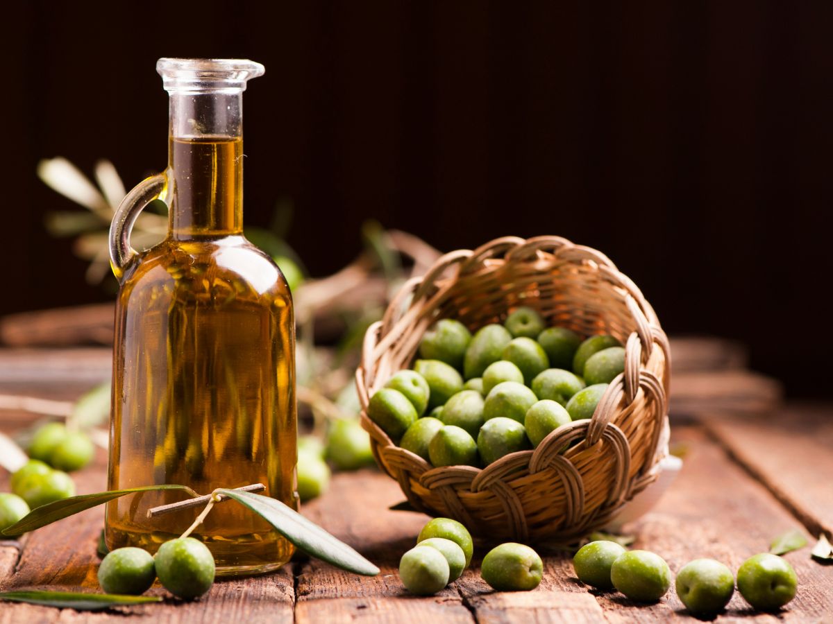 Bottle of olive oil with a small basket full of fresh olives on a table.