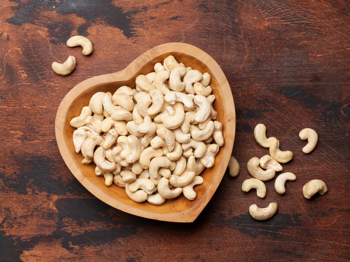A heart-shaped wooden bowl full of cashew nuts on the wooden table.