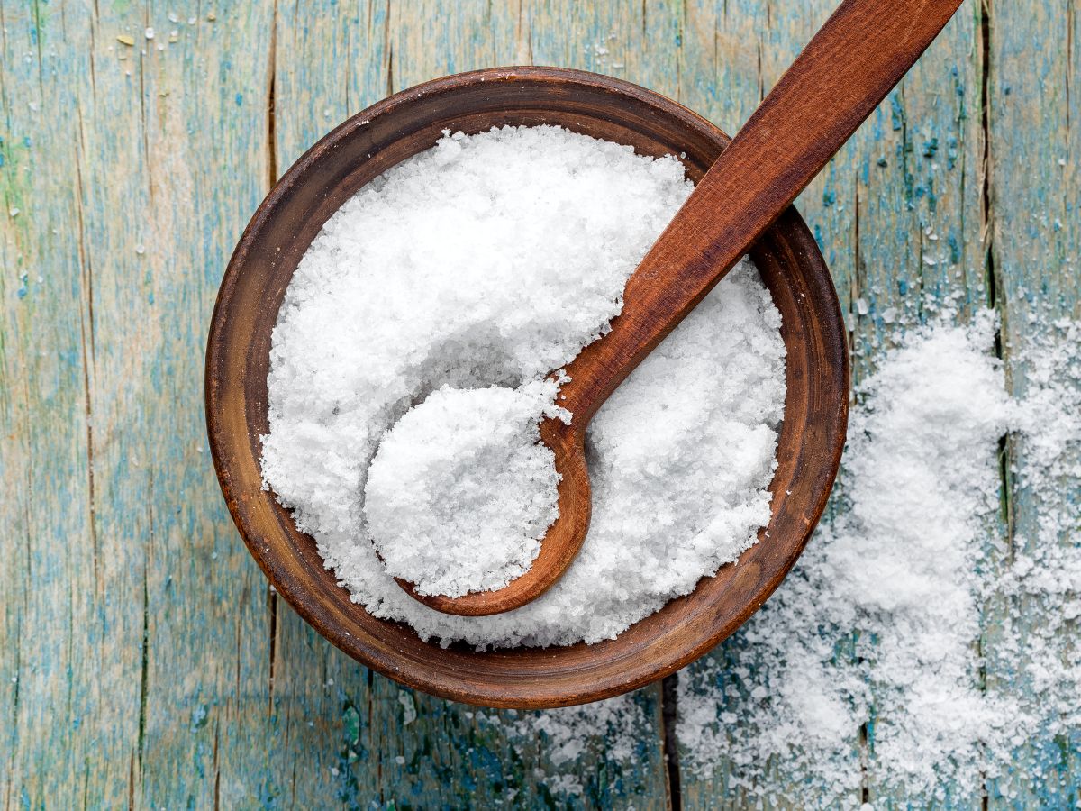 Wooden bowl full of salt with a spatula on a wooden table.