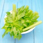 Bowl of fresh celery on a blue wooden table.