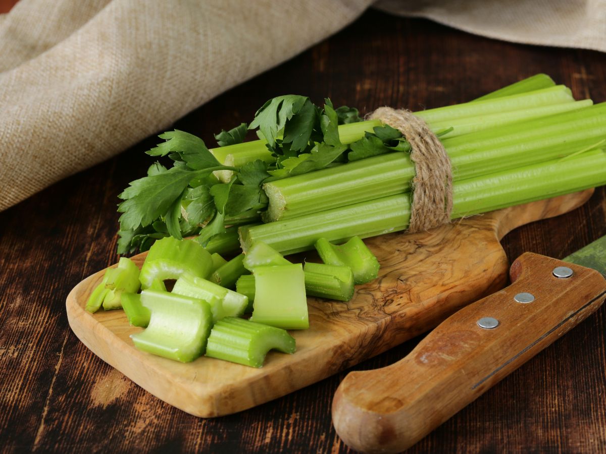 Chopped celery on a wooden cutting board with a knife on a table.