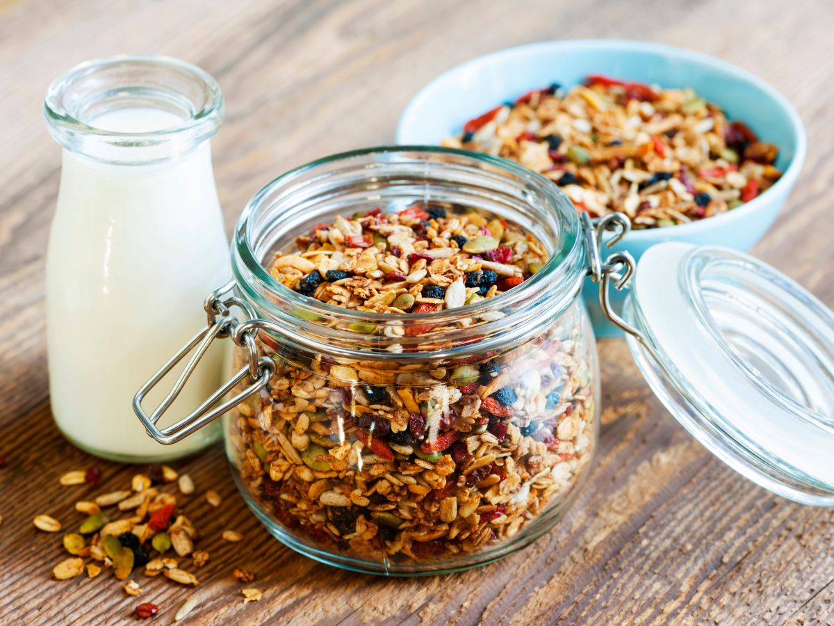 Glass jar and a bowl full of homemade granola next to a glass jar of yogurt on a table.