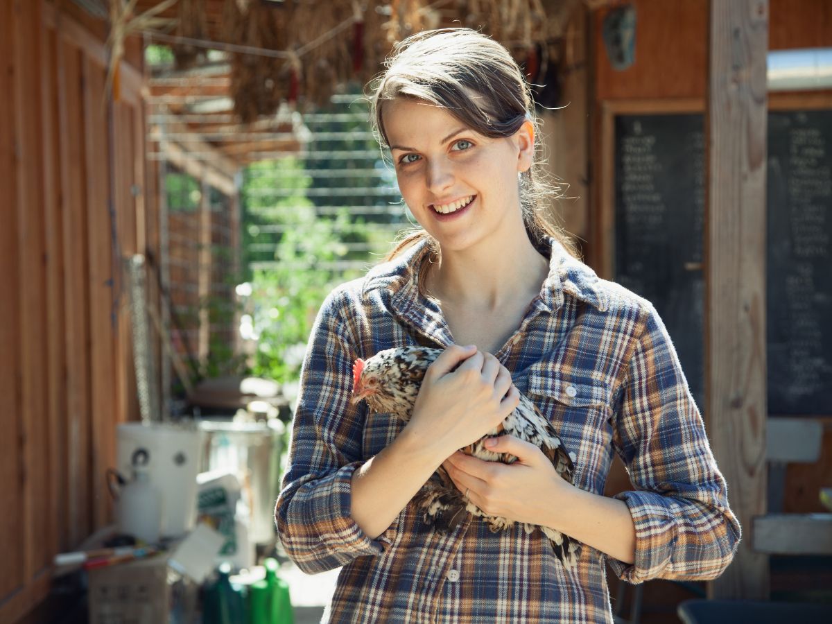 Young woman holding a chicken in her hands.