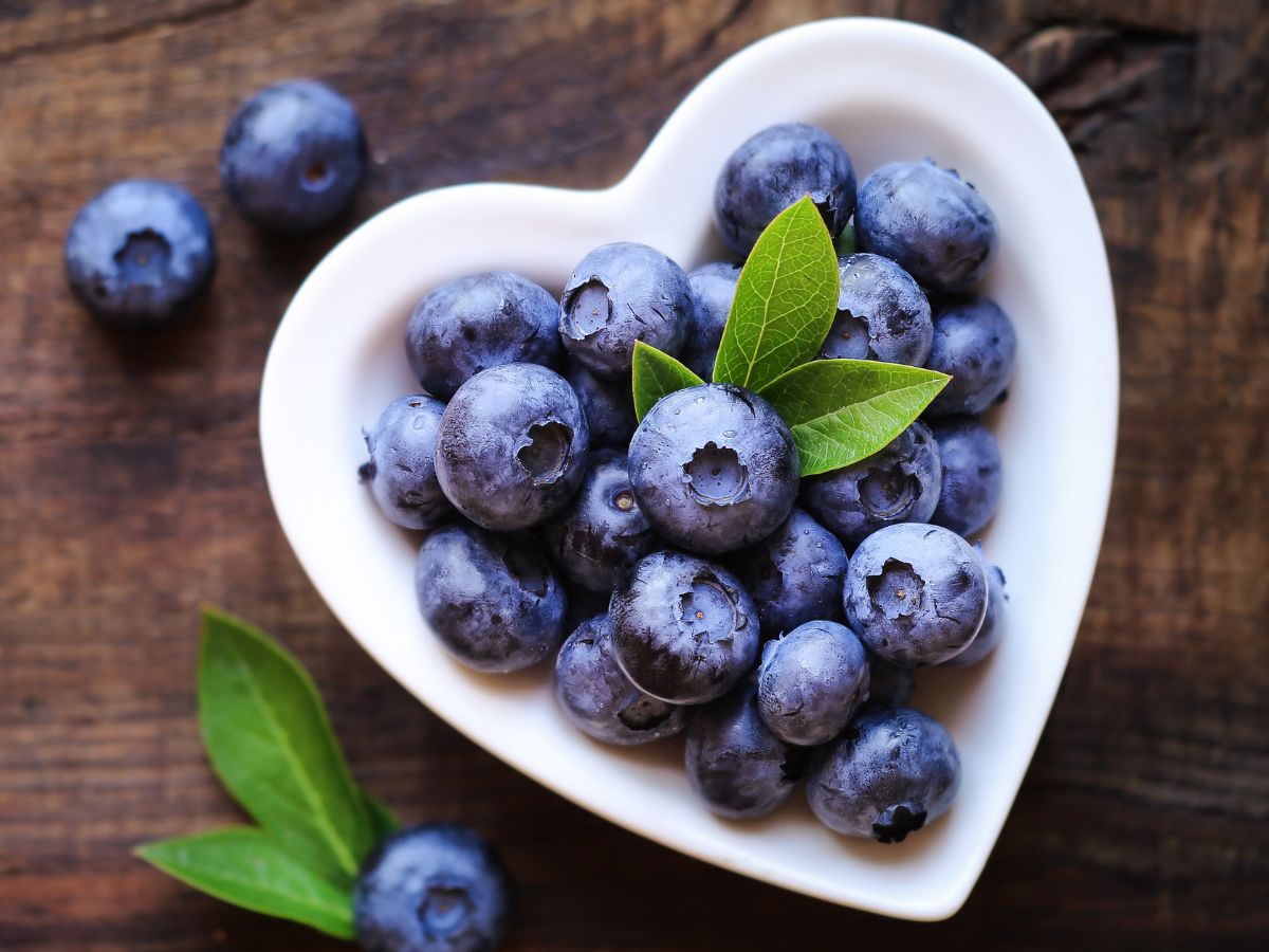 A heart-shaped white bowl full of ripe blueberries on a table.