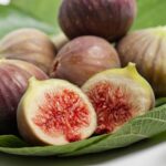 Bunch of whole and sliced ripe figs on leaves.