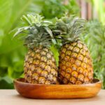 Two ripe pineapples in a wooden bowl.