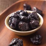 Wooden bowl of prunes on a wooden table.
