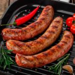 Three grilled sausages on a pan with vegetables.