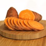 A sliced sweet potato on a wooden cutting board.