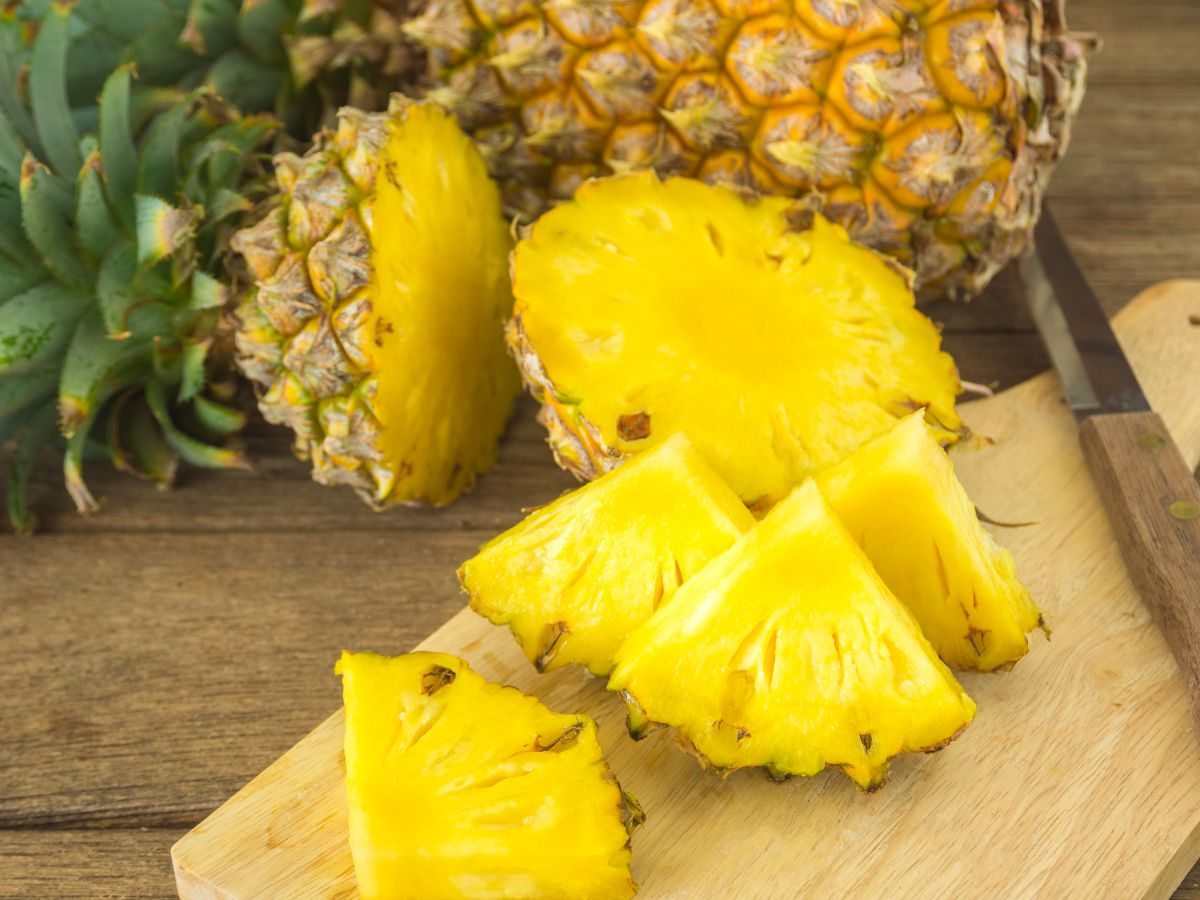 Chopped pineapple on a wooden cutting board with a knife on a table.