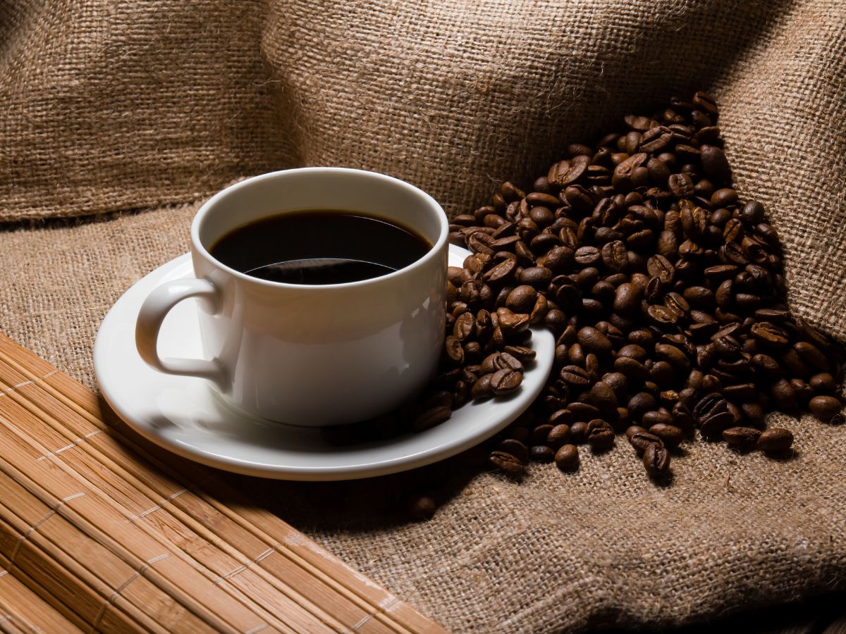 Cup of coffee on a table next to spilled coffee beans.