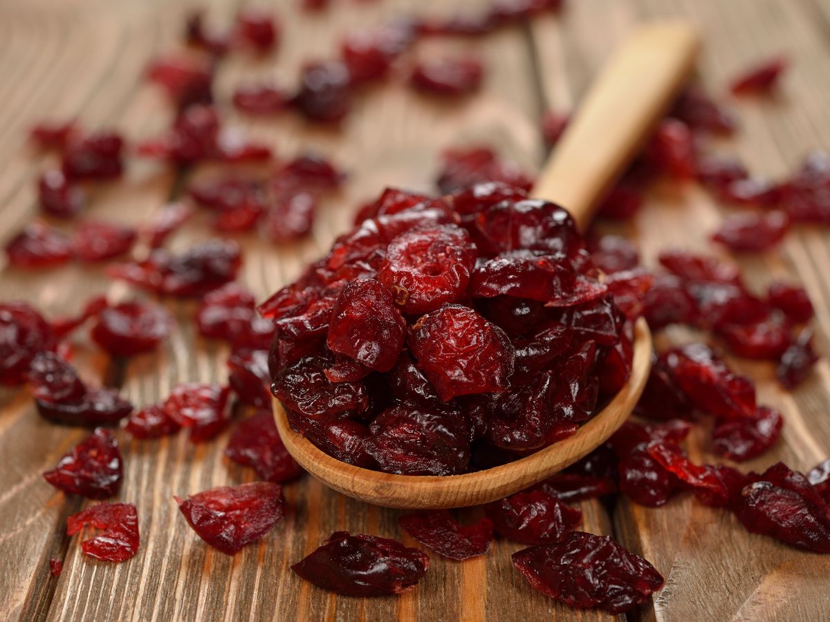 A wooden spoon full of dried cranberries on a wooden table.