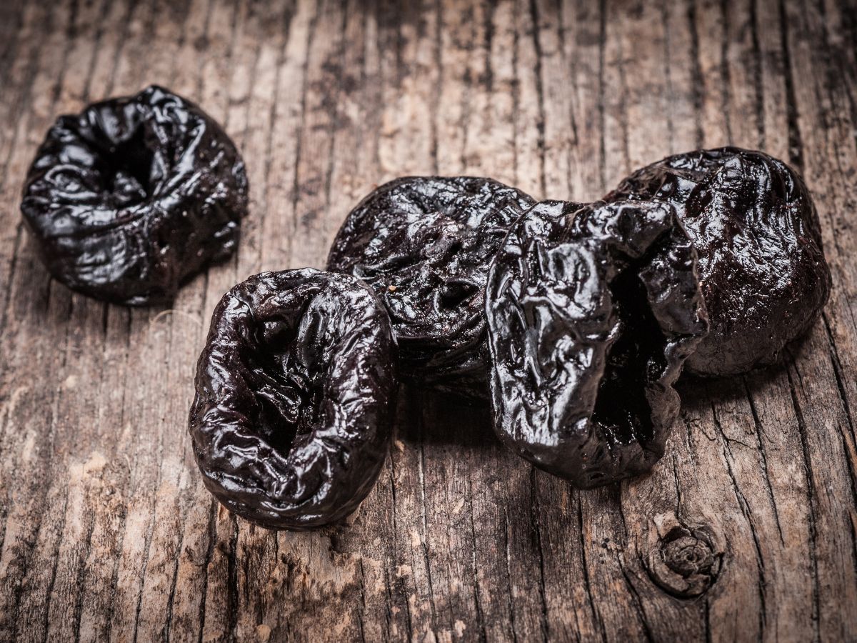 Five dried plums on a wooden board.