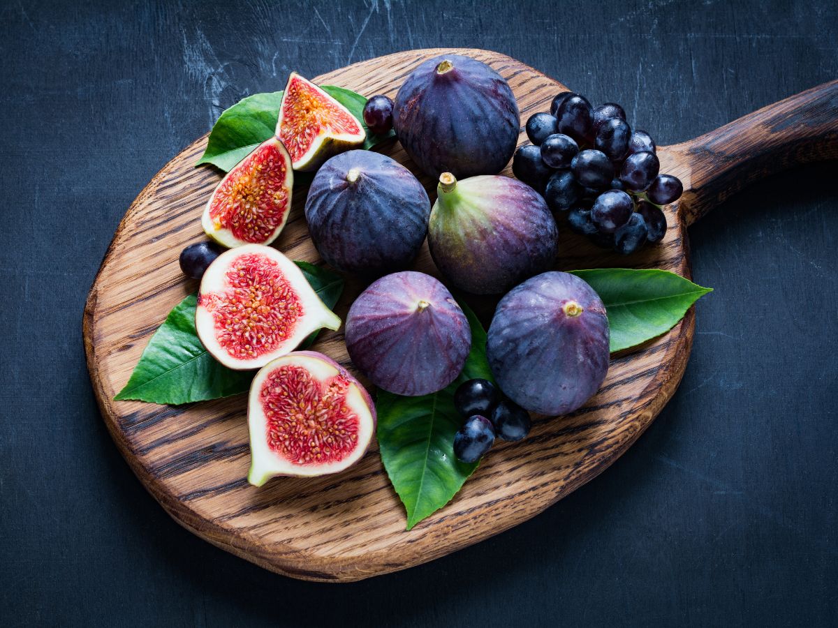 Bunch of ripe figs and grapes on a wooden cutting board.
