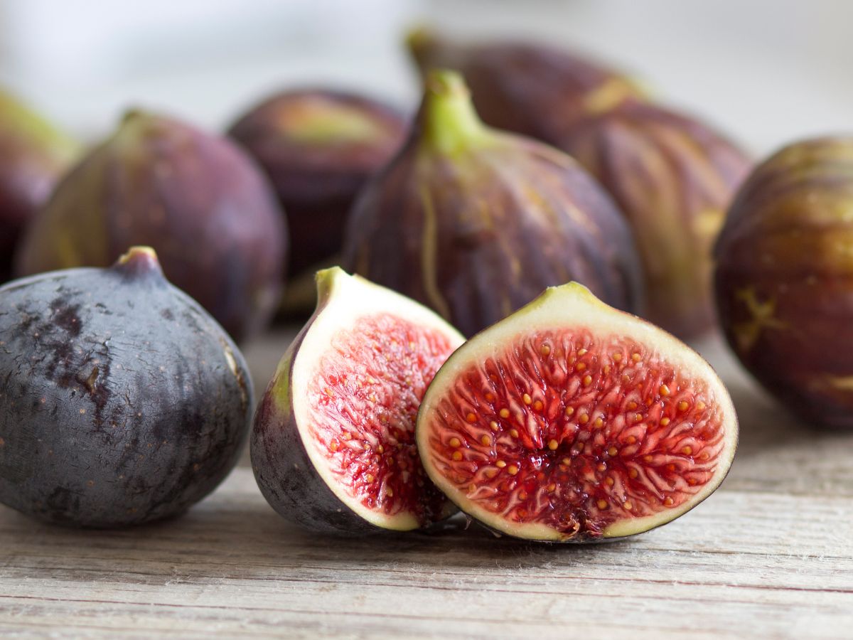 Bunch of whole and sliced figs on a wooden table.