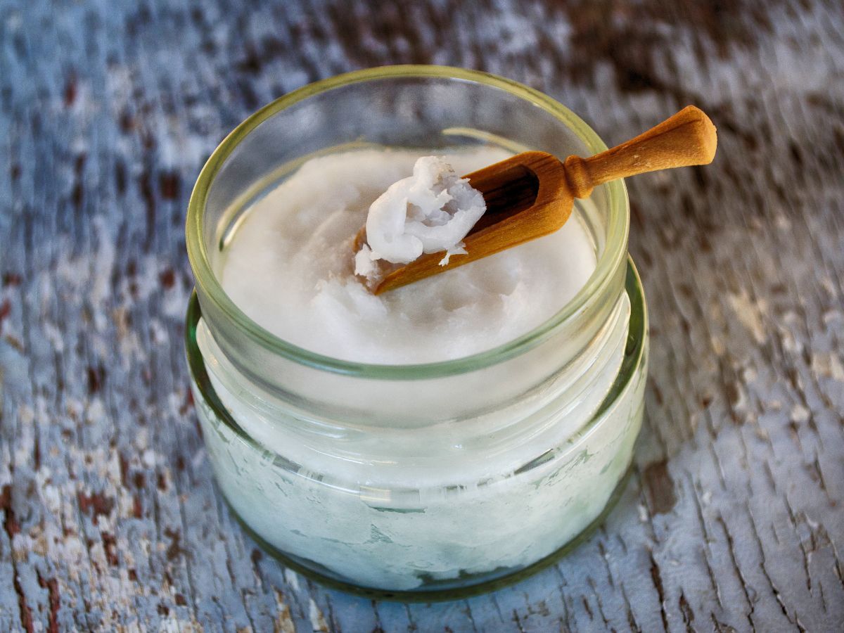 Glass jar of coconut oil with a wooden spoon on a table.