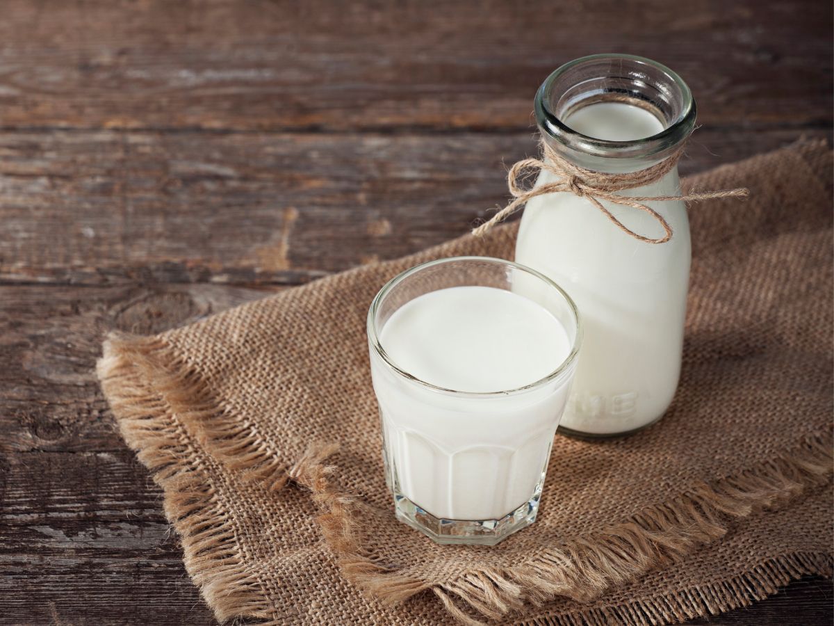 Glass jar and glass cup of milk on a wooden table.