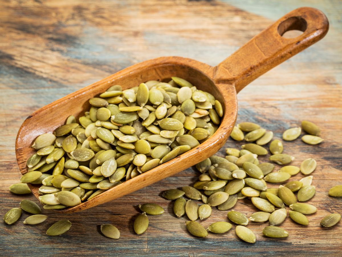 Wooden spatula full of pumpkin seeds on a table.