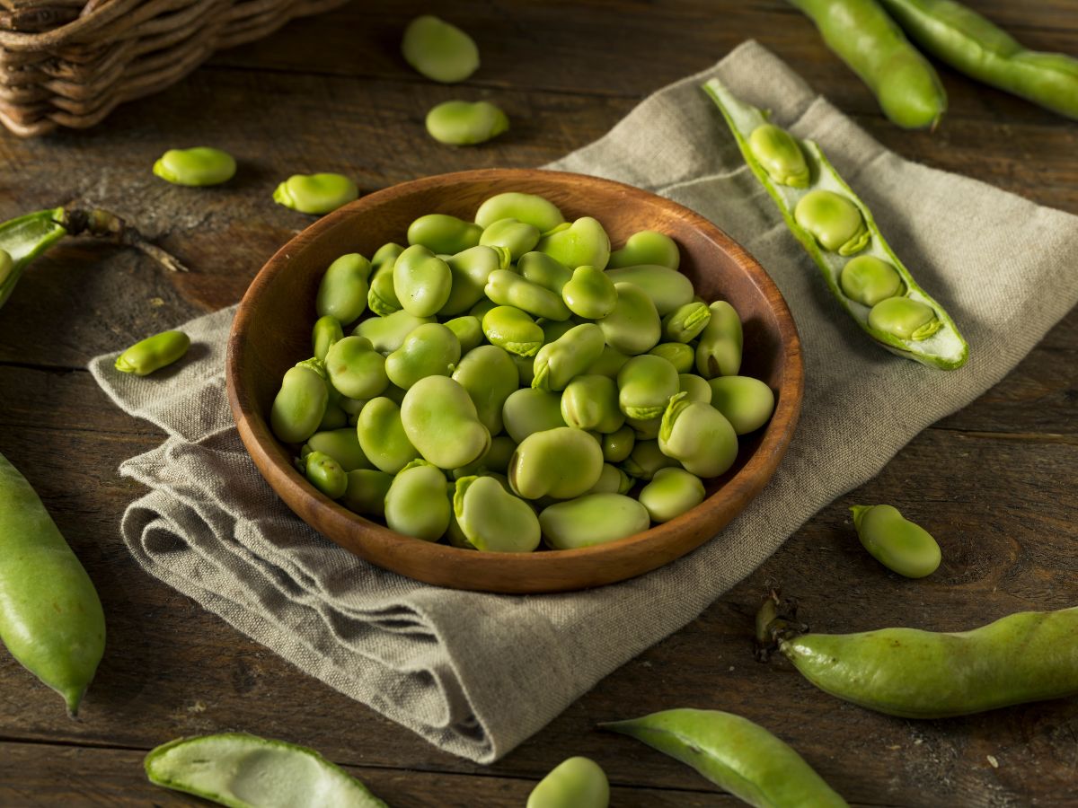 A wooden plate full of green raw beans on a wooden table.