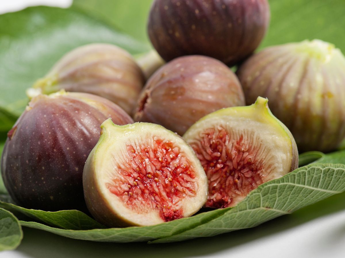 Bunch of whole and sliced figs on leaves.
