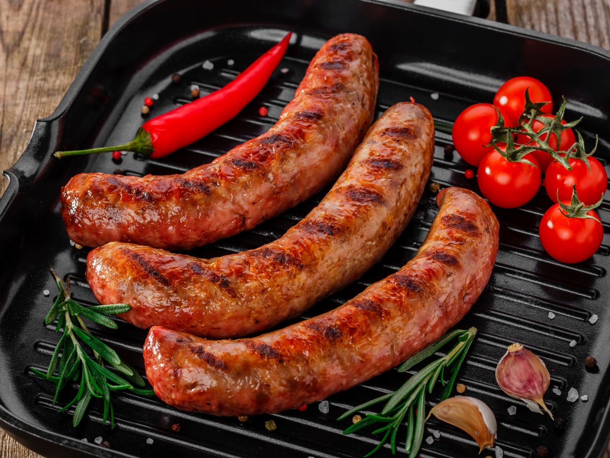 Three grilled sausages on a pan with vegetables.