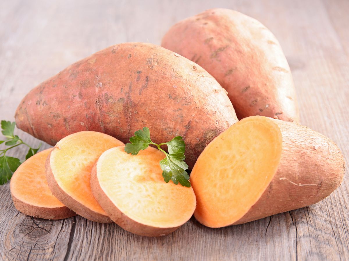 Whole and sliced sweet potatoes on a wooden table.