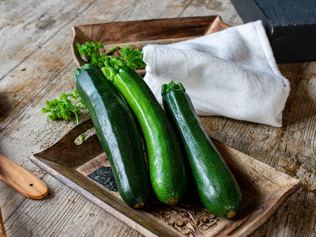 Three organic zucchinis on a wooden plate on a wooden table.