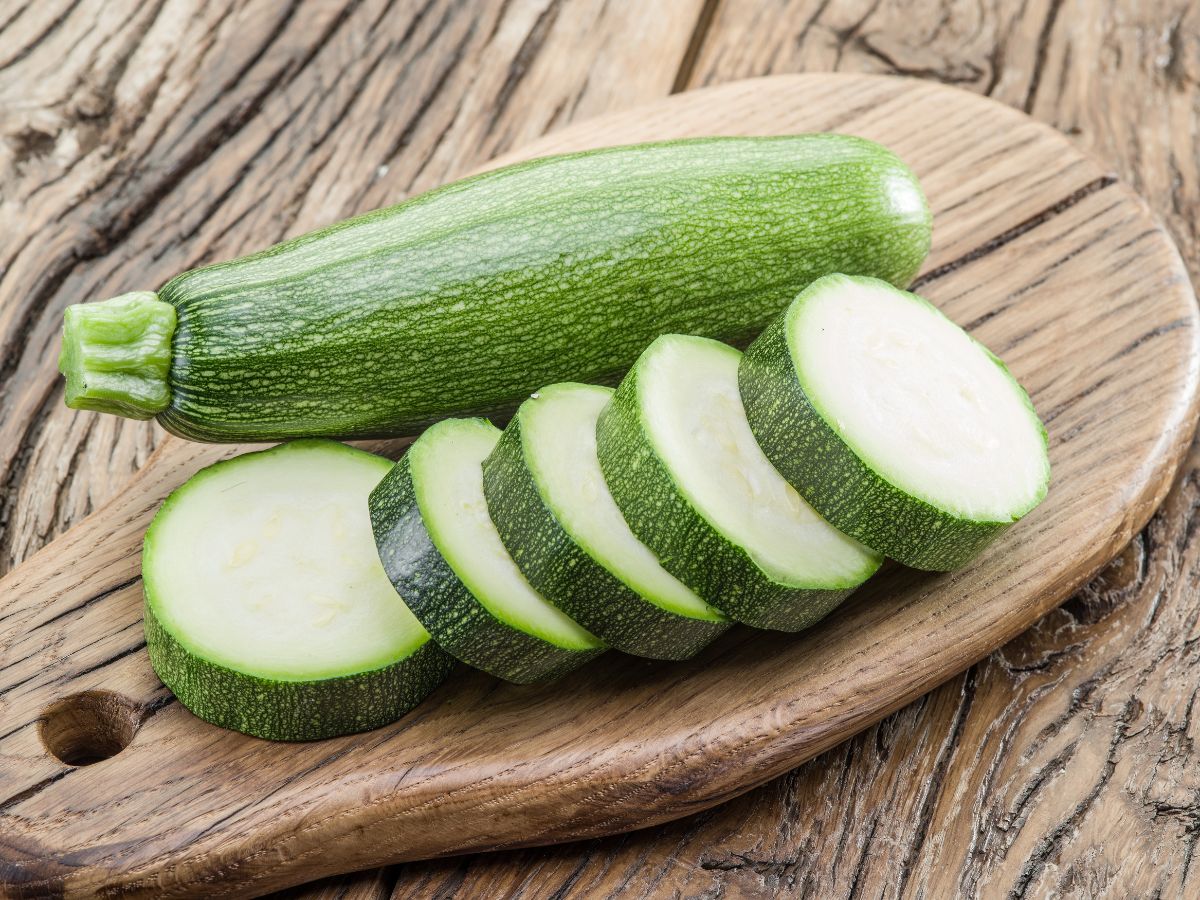 Whole and sliced zucchini on a wooden cutting table on a wooden table.
