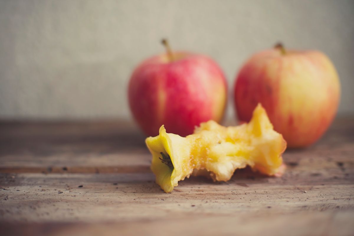 Apple core and two red apples on a wooden table.
