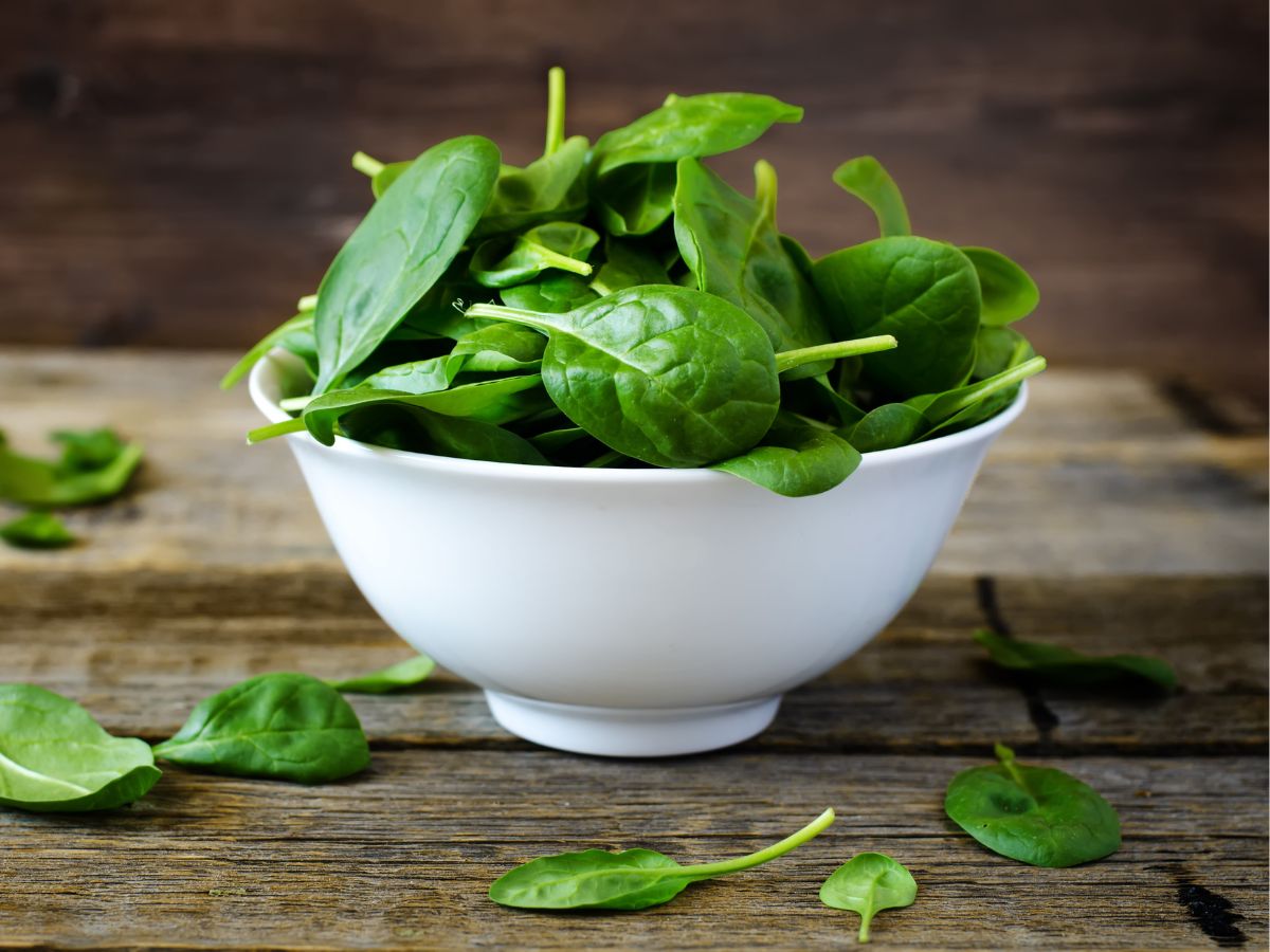White bowl of organic spinach on a wooden table.