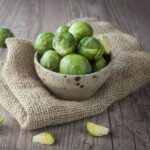 A bowl full of raw organic Brussel sprouts on a wooden table.