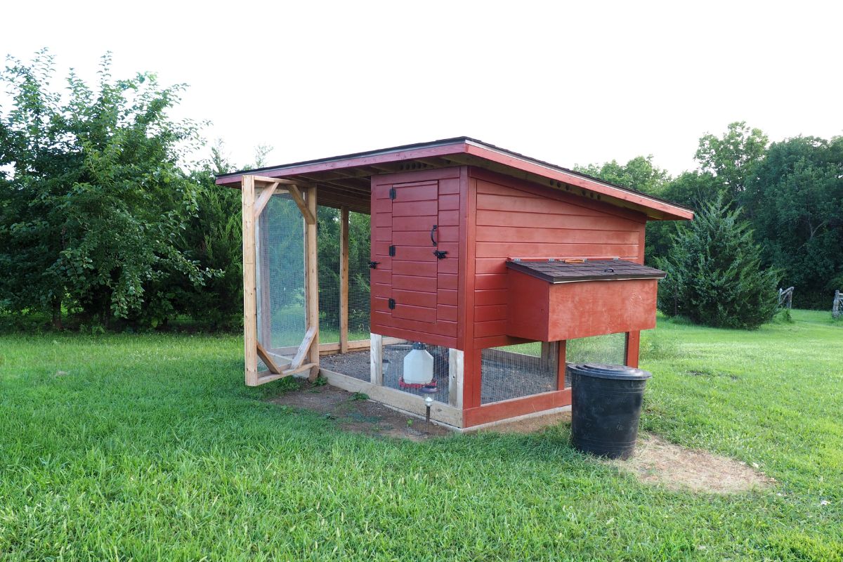 A red wooden chicken coop in a backyard.