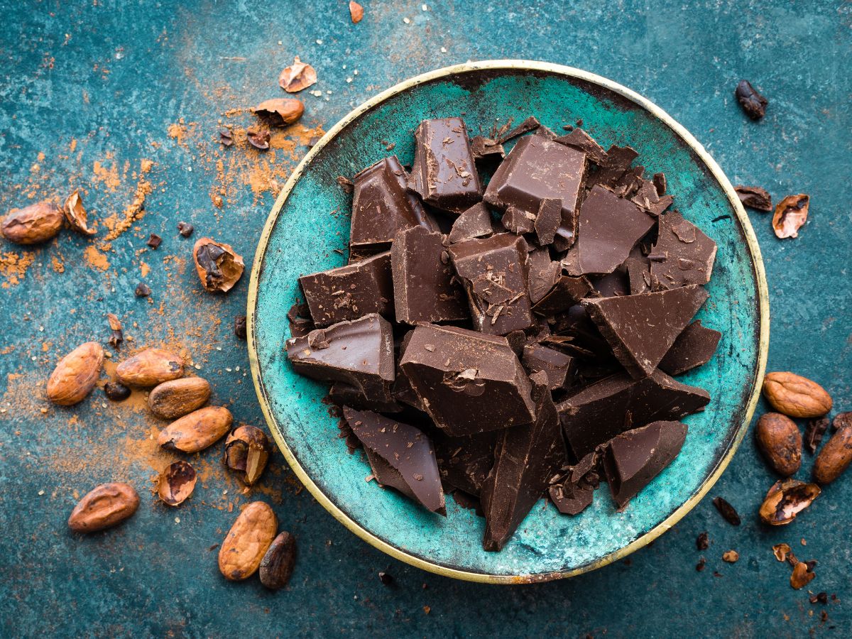 A blue plate full of chocolate pieces on a table with scattered nuts around.