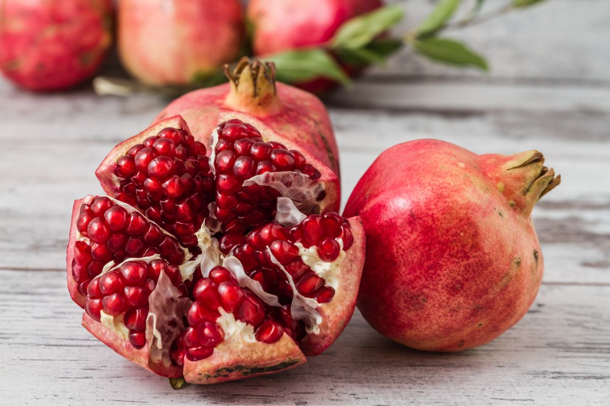 Ripe fresh, whole, and partially sliced pomegranates on a wooden table.