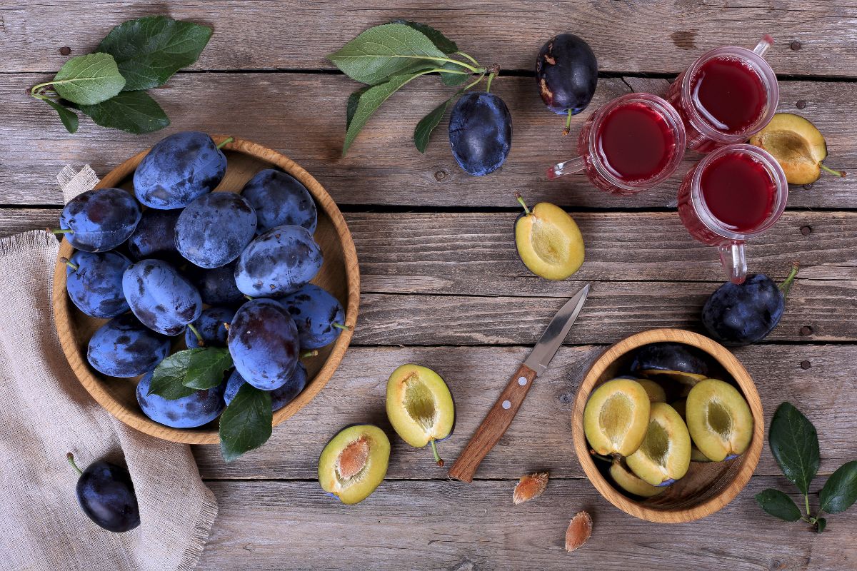 A wooden table with a bowl of plums, a knife, sliced plums, and cups of tea.