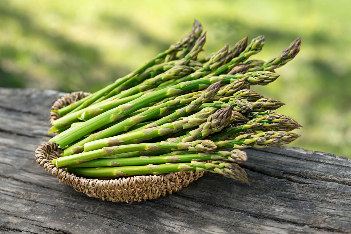 A small basket full of asparagus on a wooden board.