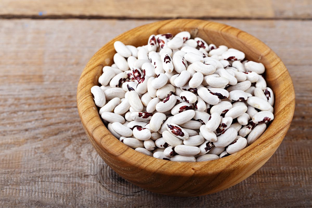 A wooden bowl of raw beans on a wooden table.