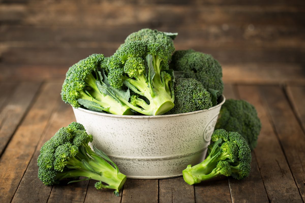 A white bowl full of fresh organic broccoli on a wooden table.