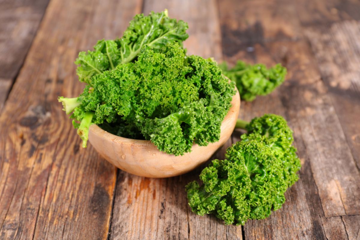 A wooden bowl of organic kale on a wooden table.