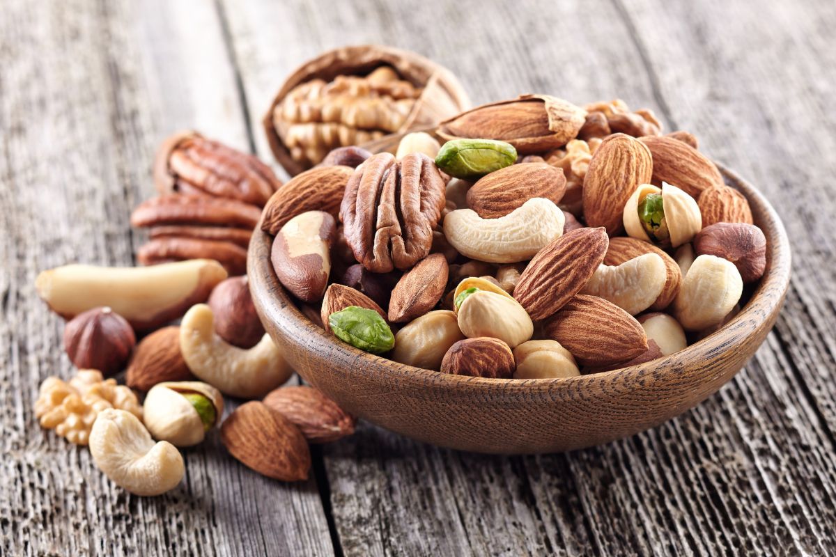 A wooden bowl of different varieties of nuts on a wooden table.