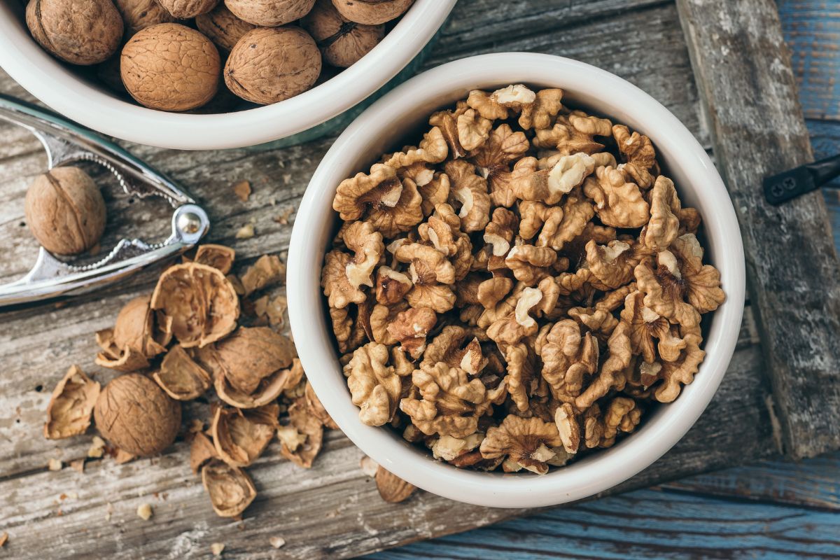 A bowl of cracked walnuts on a table with a  nutcracker and walnut shells.