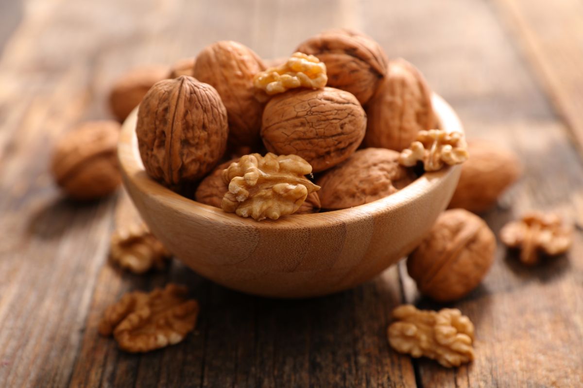A wooden bowl full of whole and cracked walnuts on a wooden table.