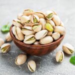 A wooden bowl full of pistachios on a table.